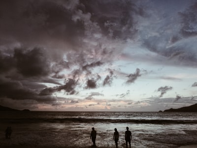 灰色多云的天空下，海边三个人的剪影